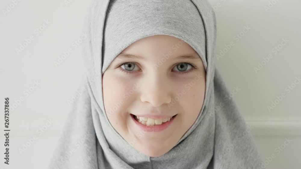 Portrait of young attractive muslim 9-years girl wearing grey hijab and traditional dress looking at the camera and smiling, close-up Portrait of young attractive muslim 9-years girl wearing grey hijab and traditional dress looking at the camera and smiling, close-up