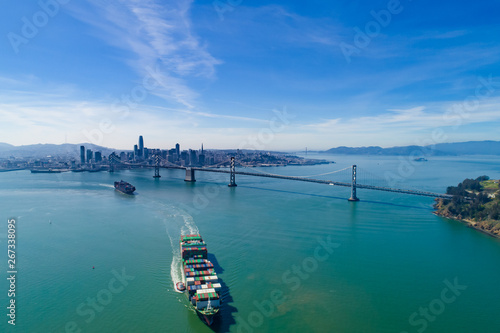 Cargo ships with containers navigating the San Francisco bay with the Bay Bridge and the city background