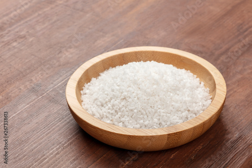A closeup photo of a bowl of sea salt on a dark rustic wooden background