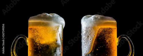 Two large glasses of beer with foam close-up, facing each other, isolated against a black background. Two overflowing glasses of beer with flowing foam.