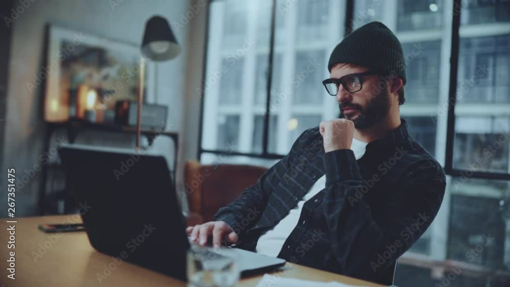 Bearded hipster working into process of startup project creating in coworking space. Man wearing eye glasses and using laptop at office