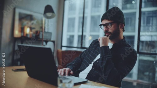 Bearded hipster working into process of startup project creating in coworking space. Man wearing eye glasses and using laptop at office