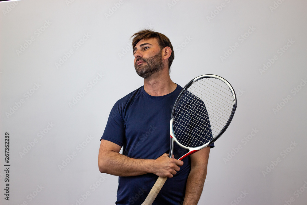 Portrait of handsome young man playing tennis holding a racket with brown hair bored, facing forwards and looking at the horizon. Isolated on white background.