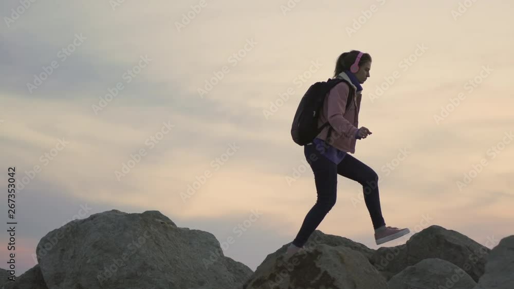 Young girl traveler walking along a ridge. Steep mountain, offering a beautiful view of the ocean at sunset Young girl traveler walking along a ridge. Steep mountain, offering a beautiful view of the ocean at sunset
