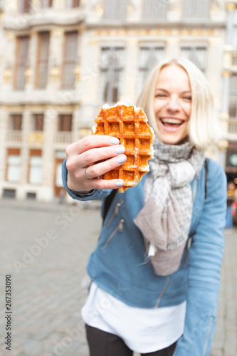 Young beautiful woman holding a traditional Belgian waffle on the background of the Great Market Square in Brussels  Belgium