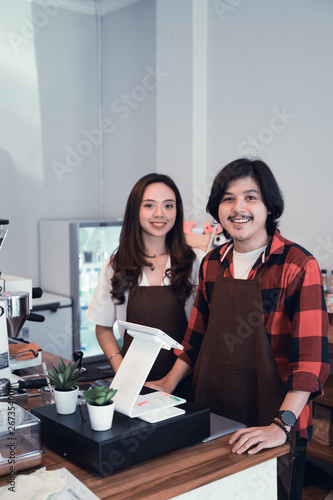 young barista and partner smiling to camera. confident couple cafe worker or owner
