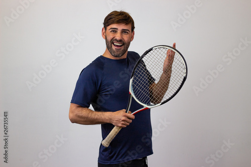 Portrait of handsome young man playing tennis holding a racket with brown hair excited, their back facing the camera and looking at the camera. Isolated on white background.