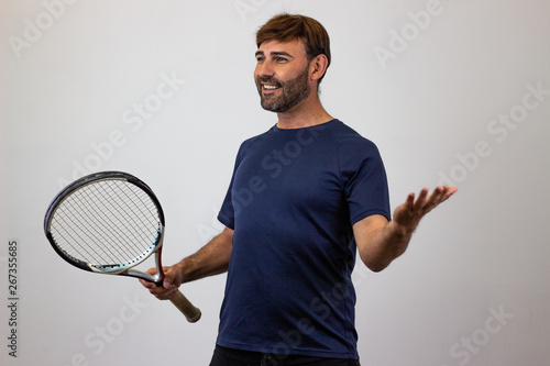 Portrait of handsome young man playing tennis holding a racket with brown hair excited, facing forwards and looking at the horizon. Isolated on white background.