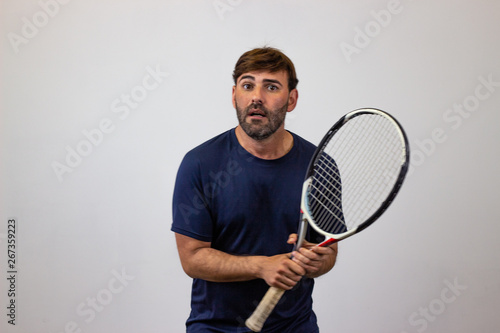 Portrait of handsome young man playing tennis holding a racket with brown hair looking jealous, looking at the camera. Isolated on white background. © Sergio Barceló