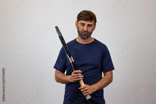 Portrait of handsome young man playing tennis holding a racket with brown hair humiliated, looking at the camera. Isolated on white background.