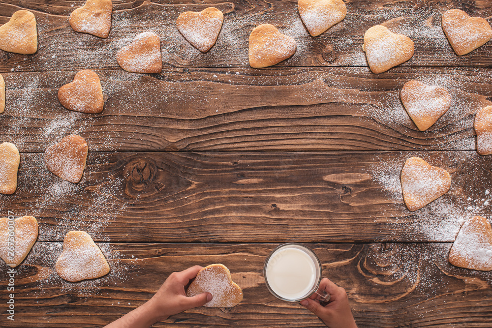 cookies heart shape sprinkled with powdered sugar on a wooden background. in the hands of biscuits and mug with milk. copy space cookies heart shape sprinkled with powdered sugar on a wooden background. in the hands of biscuits and mug with milk. copy space