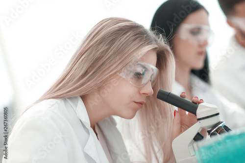 close up.serious female scientist looking into microscope in lab