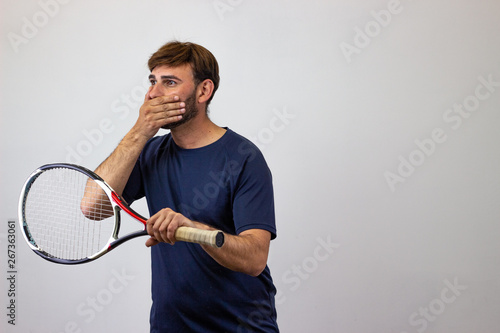 Portrait of handsome young man playing tennis holding a racket with brown hair pointing at the mouth smiling, facing forwards and looking at the horizon. Isolated on white background. © Sergio Barceló