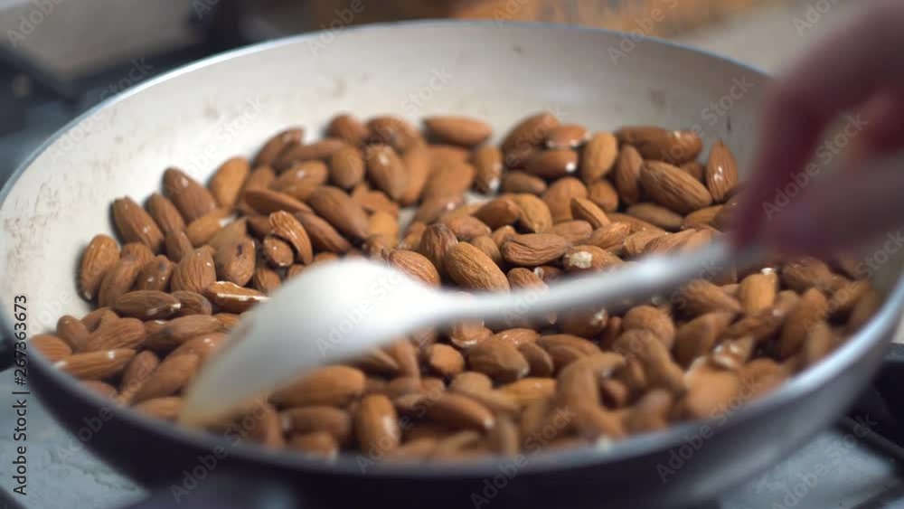 Close up, the process of frying and stirring almonds nuts in a pan on the stove, vegetarian, healthy food, diet, cooking Close up, the process of frying and stirring almonds nuts in a pan on the stove, vegetarian, healthy food, diet, cooking