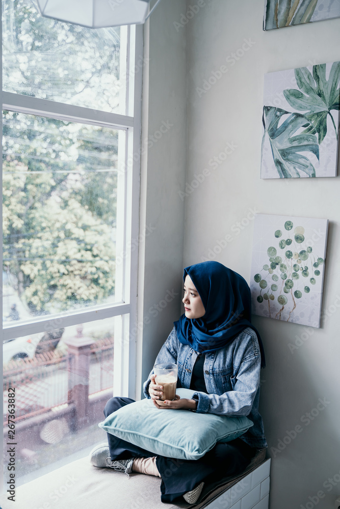 asian muslim woman enjoy relaxing sitting on couch next to window asian muslim woman enjoy relaxing sitting on couch next to window