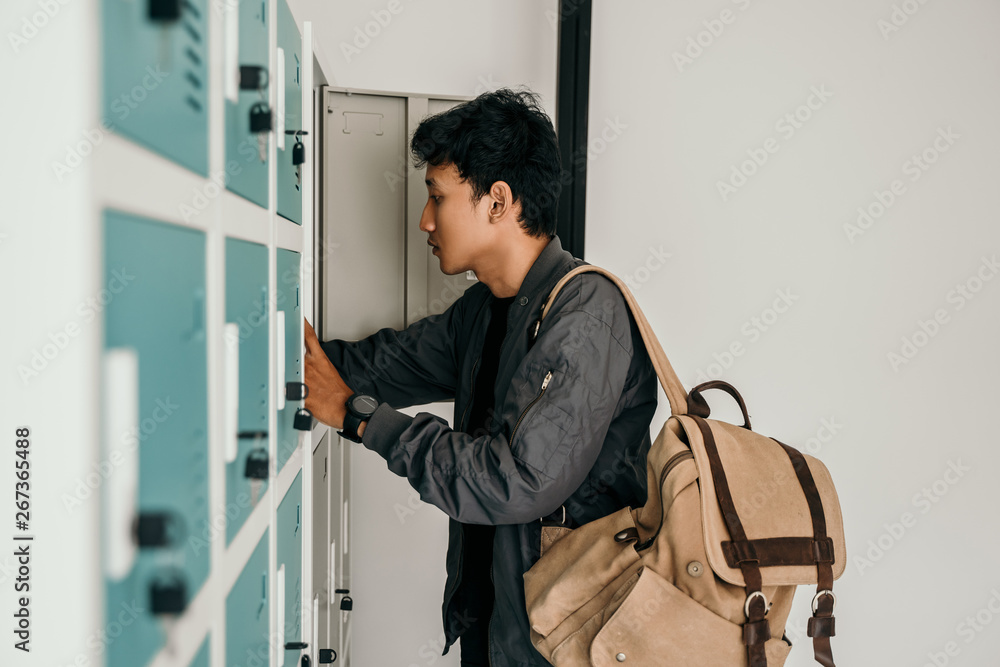 male student with bag open locker and store some stuff in it