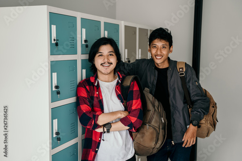 asian male young student carrying backpack in locker room smiling to camera