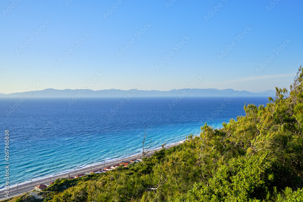 beautiful view of the sea with mountains in the background and green bushes in the foreground
