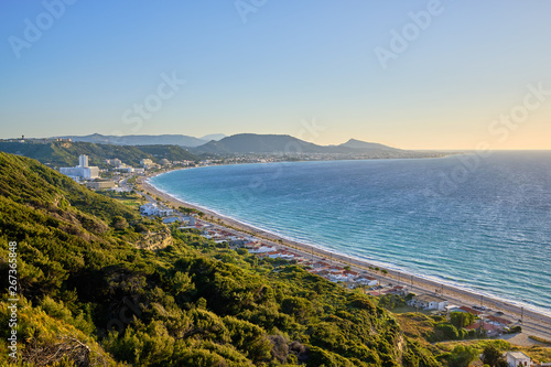 beautiful view of the sea with resort and mountains in the background and green bushes in the foreground