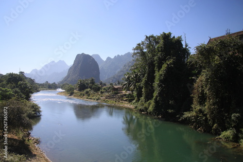 Panoramic scenic view of Nam Song (Xong) river amidst trees and rural karst hills landscape against blue clear sky , near Vang Vieng, Laos