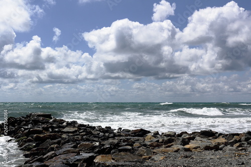 sea waves running on a stone Cape against the sky with white clouds