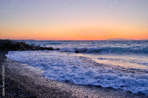 waves with foam on the beach and sunset in the background