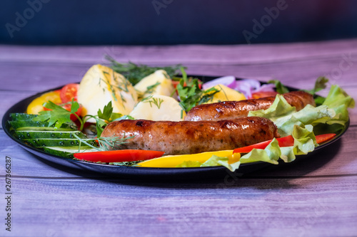 Beautiful grilled sausages on a black plate with vegetables and a background of boards.