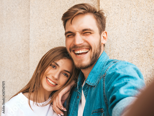 Smiling beautiful girl and her handsome boyfriend in casual summer clothes. Happy family taking selfie self portrait of themselves on smartphone camera. Having fun on the street background