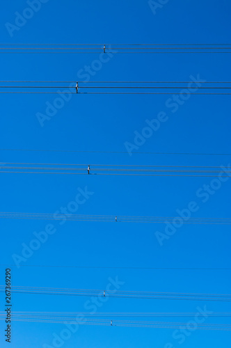 Infrastruktur, Stromleitungen und Hochspannungsleitungen mit Distanzhaltern gegen strahlend blauen Himmel