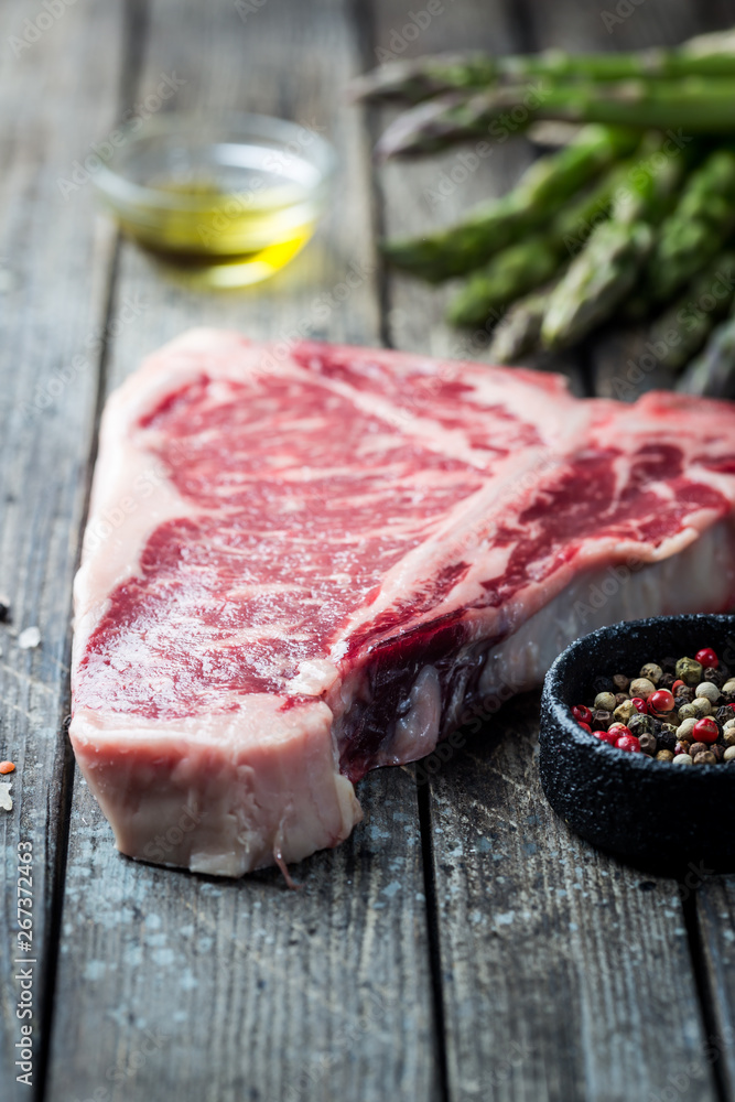 Raw T-bone Steak with fresh herbs and oil on dark wooden background Raw T-bone Steak with fresh herbs and oil on dark wooden background
