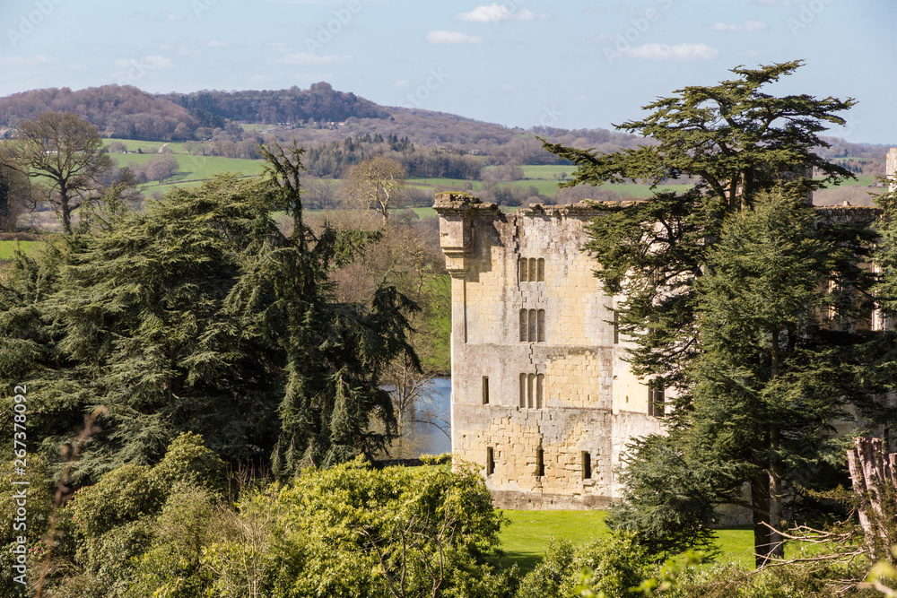 Wardour Castle, near Salibsury in Wiltshire, framed by trees on a bright sunny spring day and surrounded by lush green English countryside hills and farmland