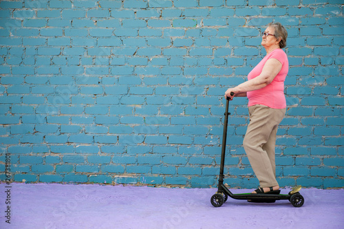 elderly woman in pink T-shirt and glasses is learning to ride new scooter. concept of an active lifestyle, sports