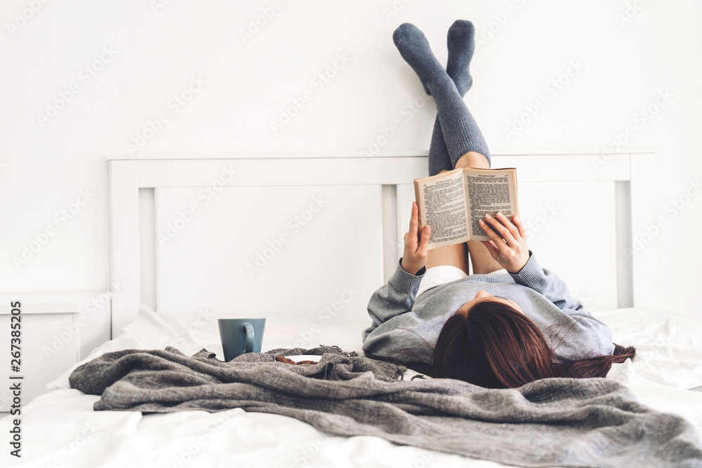 Young woman relaxing and reading book on bed at home - obrazy, fototapety, plakaty 