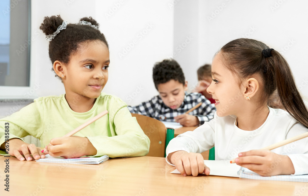 Girls at desk in classroom, looking at each other, posing. Girls at desk in classroom, looking at each other, posing.