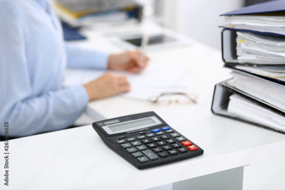 Calculator and binders with papers are waiting to be processed by business woman or bookkeeper back in blur. Internal Audit and tax concept Calculator and binders with papers are waiting to be processed by business woman or bookkeeper back in blur. Internal Audit and tax concept