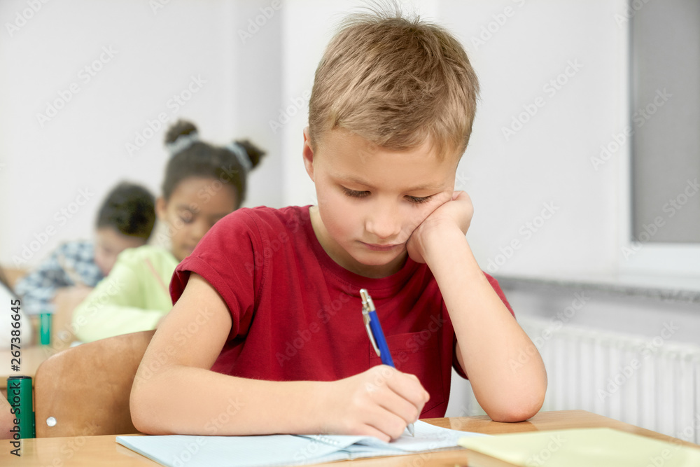 Schoolboy at desk writing with pen in copybook. Schoolboy at desk writing with pen in copybook.