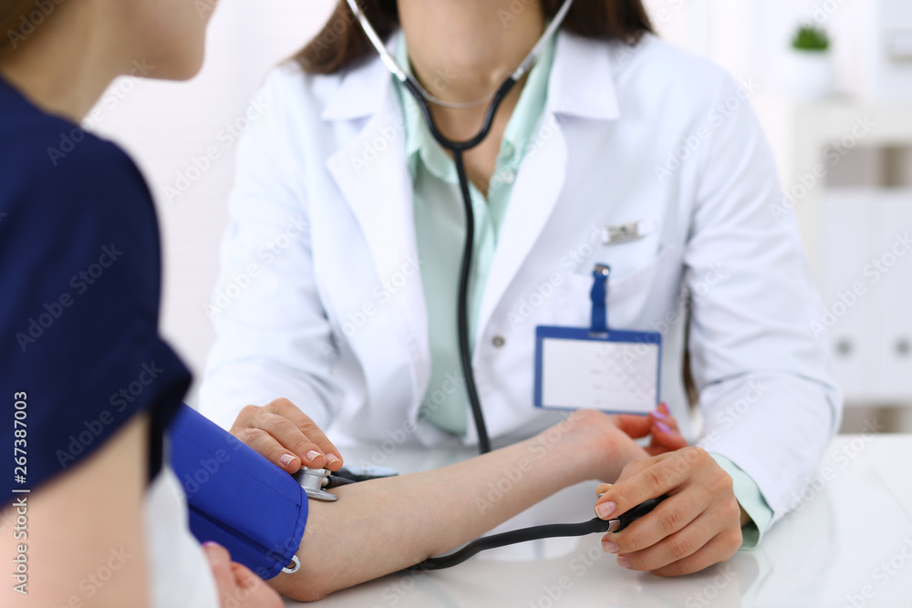 Unknown doctor woman checking blood pressure of female patient, close-up. Cardiology in medicine and health care concept Unknown doctor woman checking blood pressure of female patient, close-up. Cardiology in medicine and health care concept