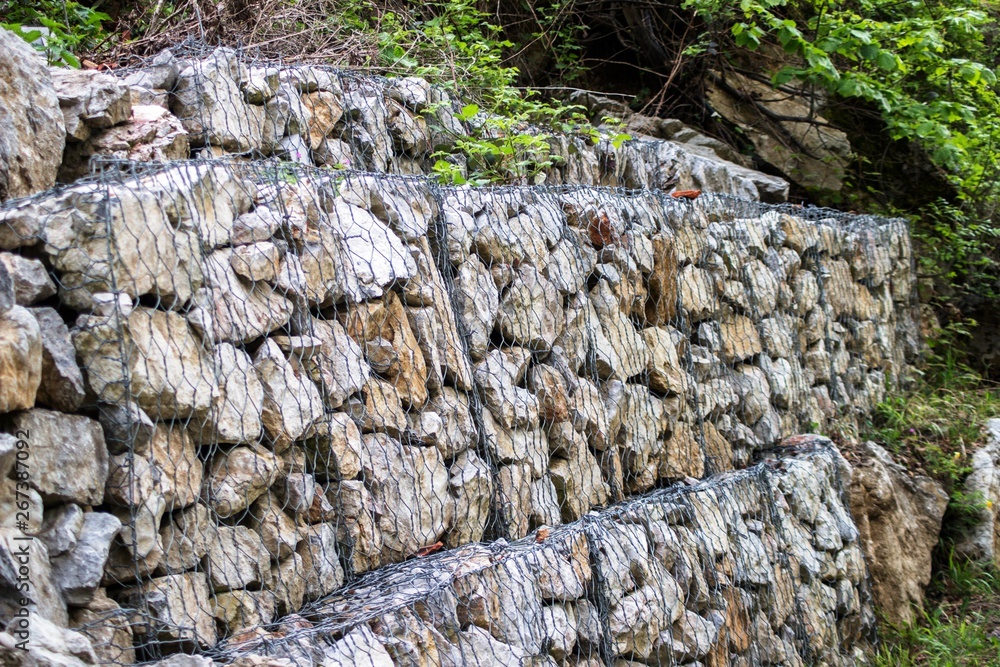 Retaining stone wall next to the road.Steel mesh of gabion wall.