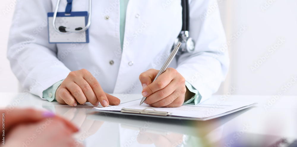 Doctor and patient talking while sitting at the desk in hospital office, close-up of human hands. Medicine and health care concept Doctor and patient talking while sitting at the desk in hospital office, close-up of human hands. Medicine and health care concept