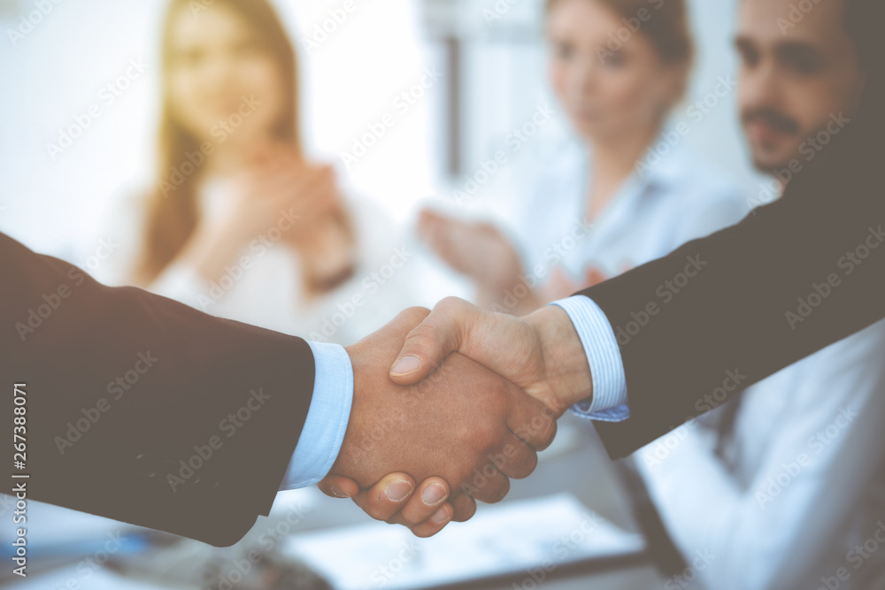 Business people shaking hands at meeting while theirs colleagues clapping and applauding. Group of unknown businessmen and women in modern white office. Success teamwork, partnership and handshake Business people shaking hands at meeting while theirs colleagues clapping and applauding. Group of unknown businessmen and women in modern white office. Success teamwork, partnership and handshake