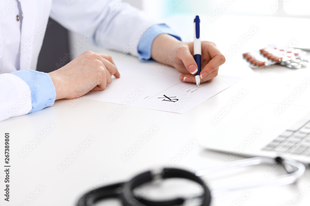 Female doctor filling up prescription form while sitting at the desk in hospital closeup. Healthcare, insurance and excellent service in medicine concept Female doctor filling up prescription form while sitting at the desk in hospital closeup. Healthcare, insurance and excellent service in medicine concept