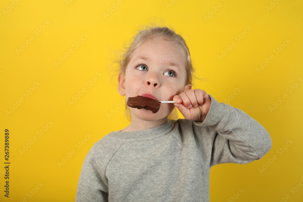 Cute girl child eating sweet chocolate candy on yellow background. Happy childhood.