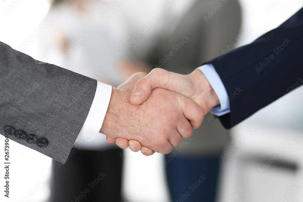 Business people shaking hands at meeting or negotiation, close-up. Group of unknown businessmen and women in modern office at background. Teamwork, partnership and handshake concept