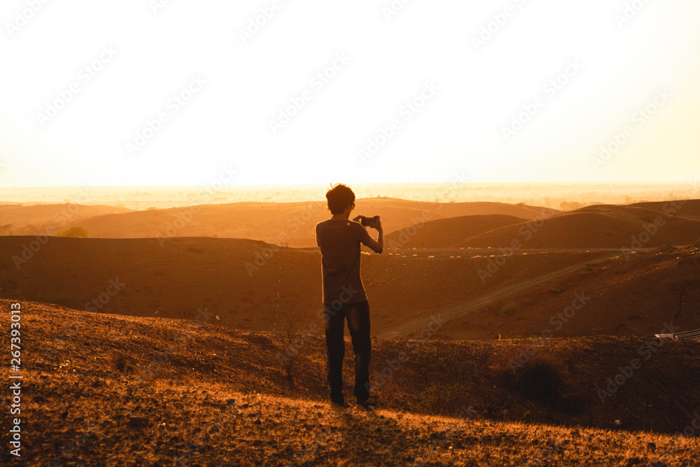 Man taking photograph of the hills using his mobile phone during the golden hour of sunset Man taking photograph of the hills using his mobile phone during the golden hour of sunset