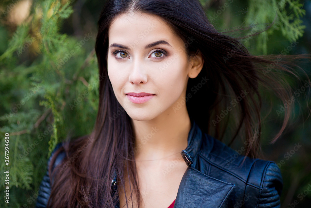 Close up outdoor portrait of young beautiful brunette woman with green eyes and long healthy hair.