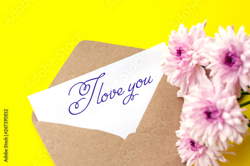 Love envelope and letter with written words I love you with pink chrysanthemum flowers on bright yellow bacground.