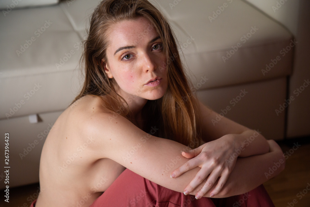 Portrait of young topless charming woman with brown hair sitting on floor and looking at camera Portrait of young topless charming woman with brown hair sitting on floor and looking at camera