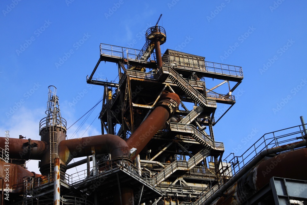 Landschaftspark Duisburg, Germany: Low angle view on stairways into deep blue sky at corroded tower with rusty pipeline