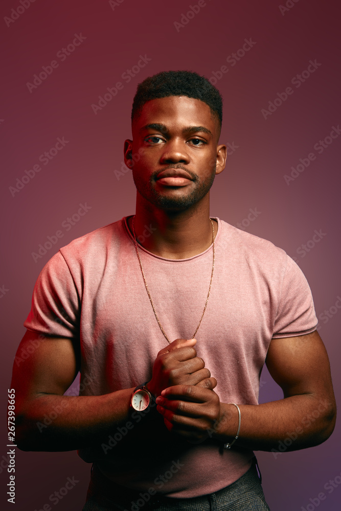 Serious black Afro American man with thoughtful expression looking directly into camera while posing against dark studio wall. Grave sportsman in t-shirt planning day schedule