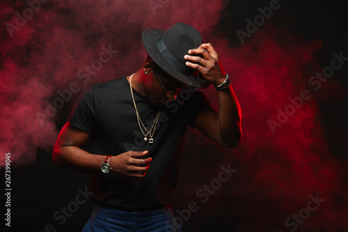Portrait of handsome young african DJ or jazz musician in creative hat in black t-shirt on dark background © alfa27